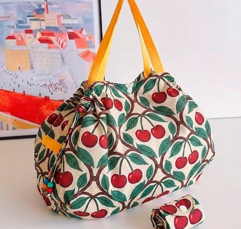Reusable grocery bag with a vintage cherry print and yellow handles next to its folded pouch.