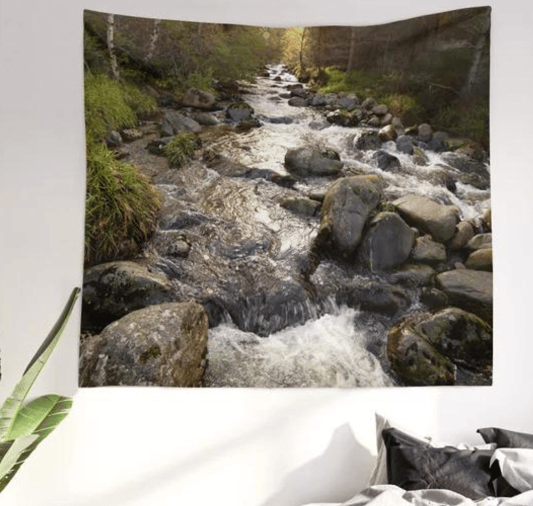 Wall tapestry on wall with autumnal river printed on it, bed in situ underneath.