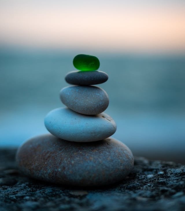 Balanced stack of smooth zen stones topped with a green sea glass piece at dusk.