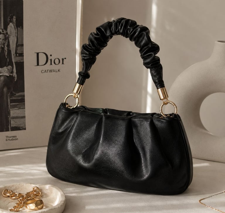 Black ruched shoulder bag with gold accents on a luxury background.