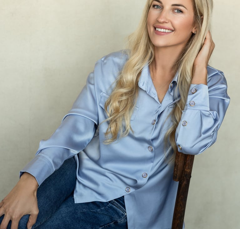 moteris human design koučerė sėdi ir šypsosi, apsirengusi žydros spalvos marškiniais