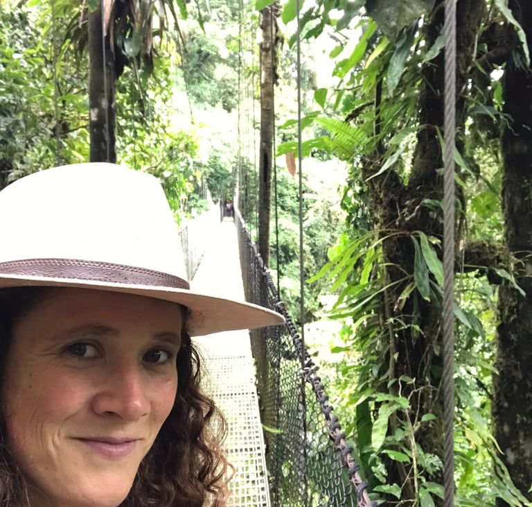 une femme aux cheveux frisés sur un pont suspendu au costa rica, un léger sourire sur les lèvres