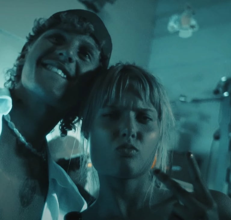 A smiling man and woman posing for a selfie in a blue-lit nightclub with a menu board.