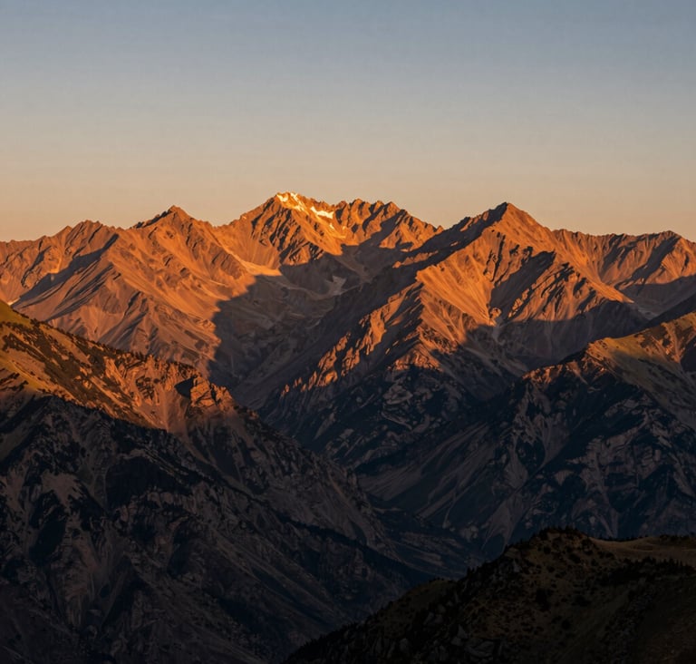 A breathtaking landscape shot of a mountain range at golden hour. The peaks are bathed in warm orange light, with charcoal shadows in the valleys. The composition is authentic and vast.