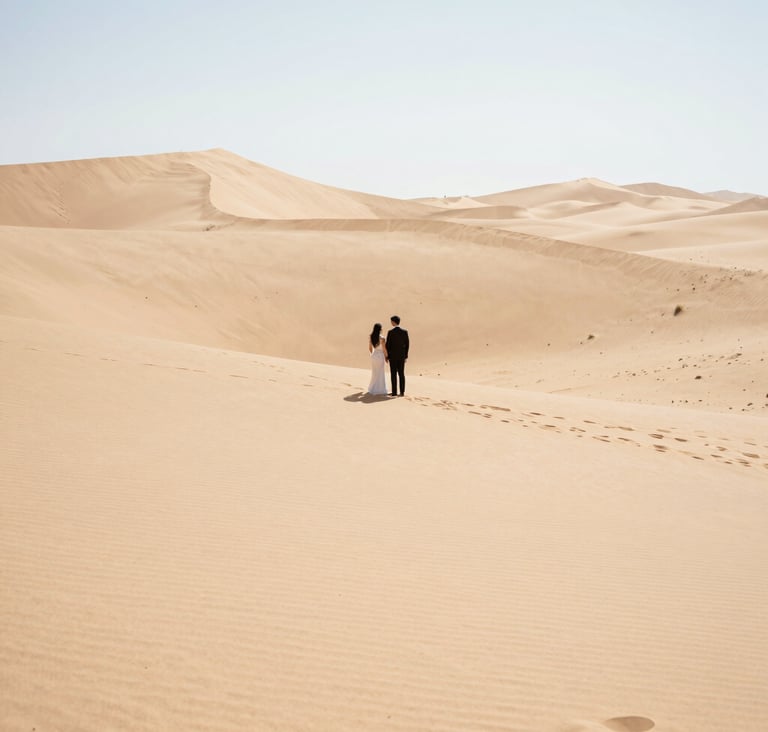 A wide-angle landscape photograph of an elopement in a North American desert. The couple is a small focal point against vast, clean lines of sand dunes. Bright, airy lighting, high-end professional photography style.