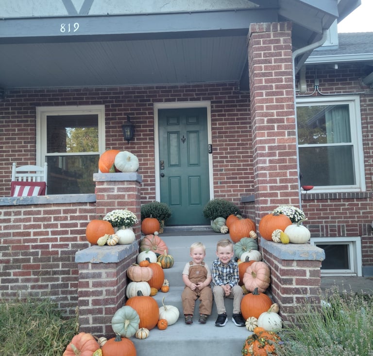 Two young boys sitting on the steps of a house surrounded by pumpkins