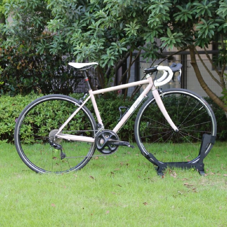 A retro pink road bike with white drop handlebars parked on a green grass lawn.