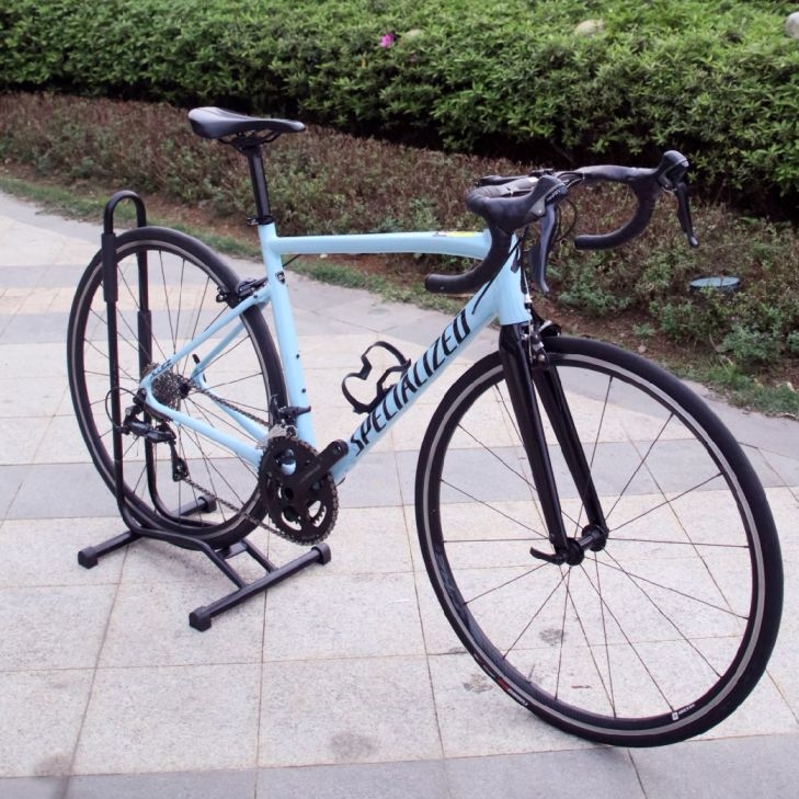Light blue Specialized Allez road bike on a display stand with carbon fiber forks and drop handlebars.