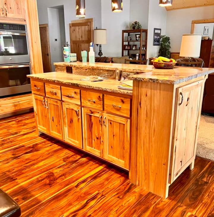 Rustic kitchen island with knotty pine cabinets and granite countertops over rich hardwood floors.