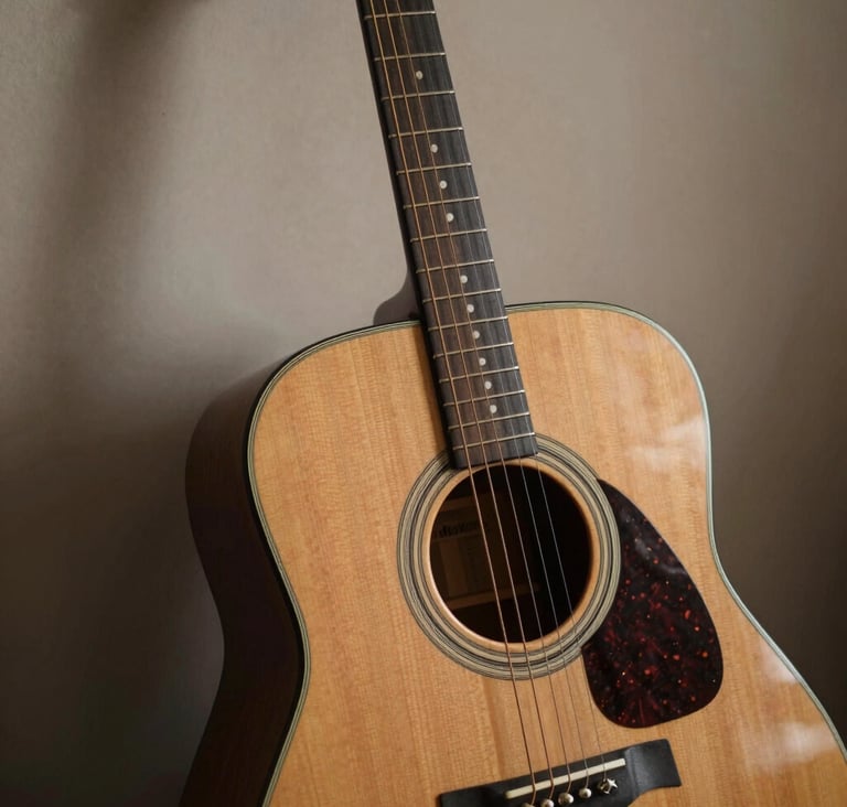 A close-up photograph of a vintage acoustic guitar leaning against a soft taupe wall in a North American / US music room. The lighting is soft and natural, highlighting the wood grain and strings. Moody dark charcoal brown shadows add depth.