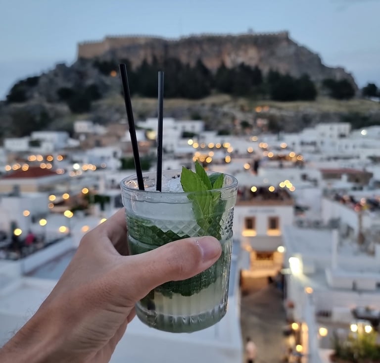 A refreshing mint mojito cocktail at a Lindos rooftop bar with the Acropolis of Rhodes in the background.