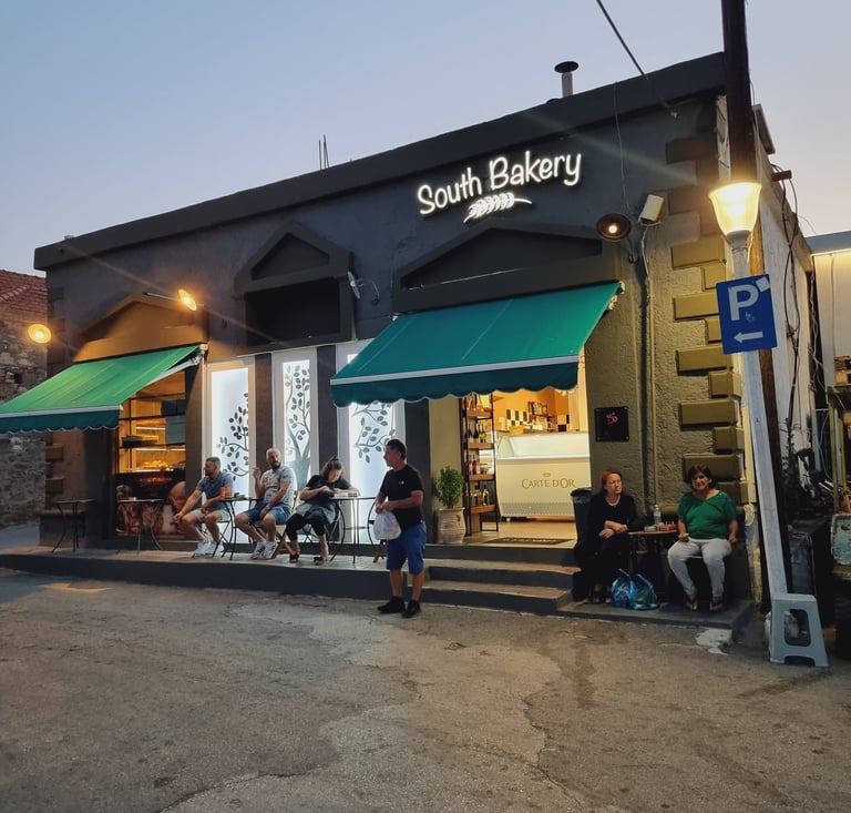 Customers sitting outside the South Bakery storefront with green awnings at dusk.