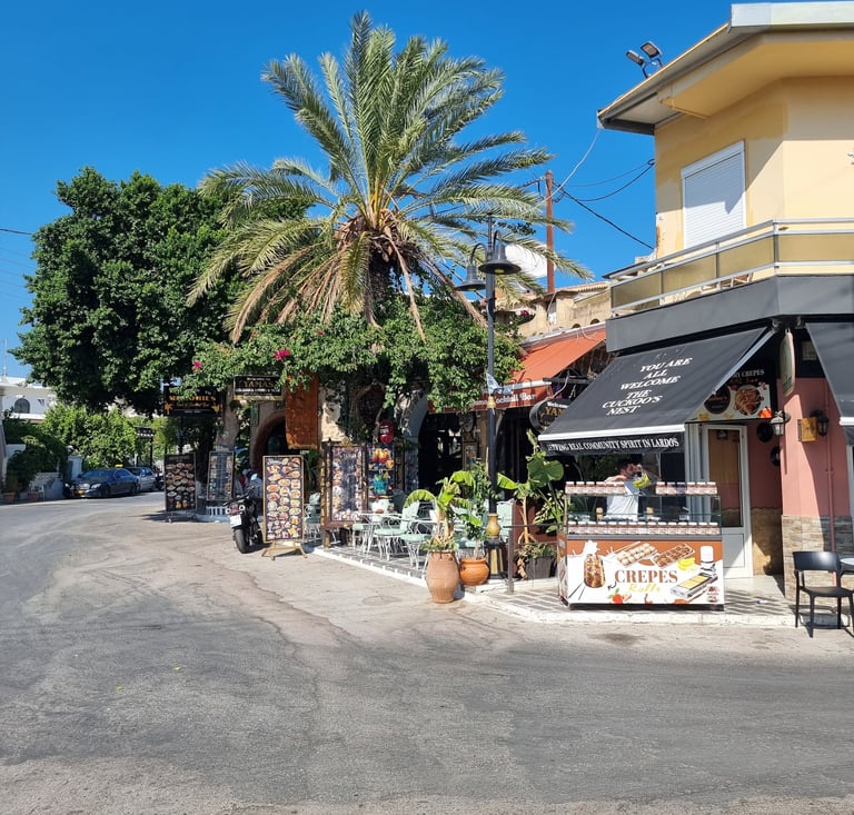 Crepes stall and sidewalk cafe with palm trees on a sunny street in Lardos, Rhodes.