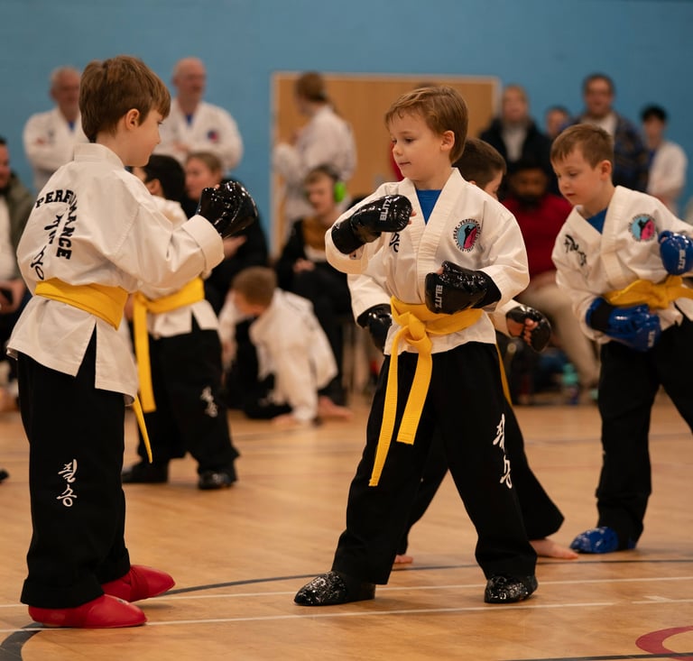 Young children in white uniforms and yellow belts practice karate sparring in a martial arts class.