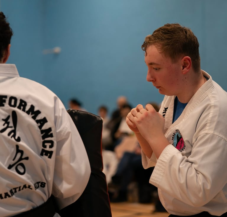 A young martial artist in a white taekwondo uniform practicing punches with a training partner.