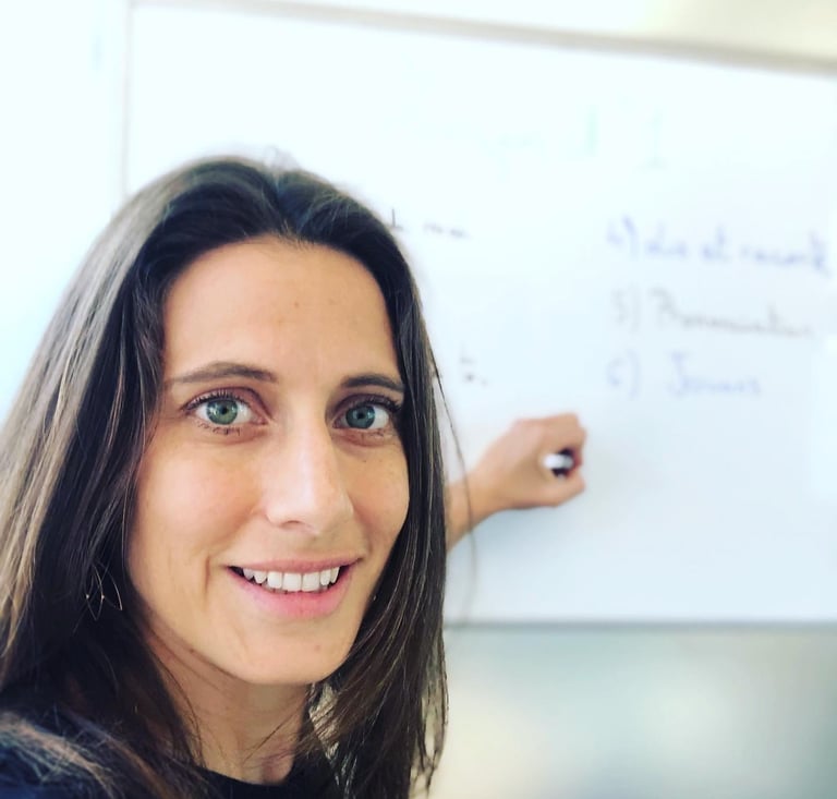 a woman French teacher standing in front of a white board she tutors French class