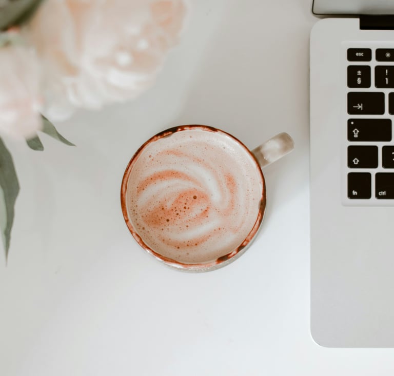 un espace bureau appaisant pourvu d'une tasse de café, des fleurs roses pales et un clavier d'ordinateur