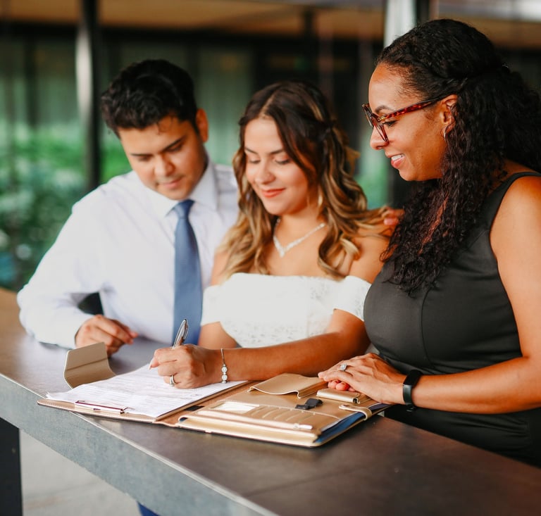 A bride and groom signing their marriage certificate with a wedding officiant at an outdoor ceremony.