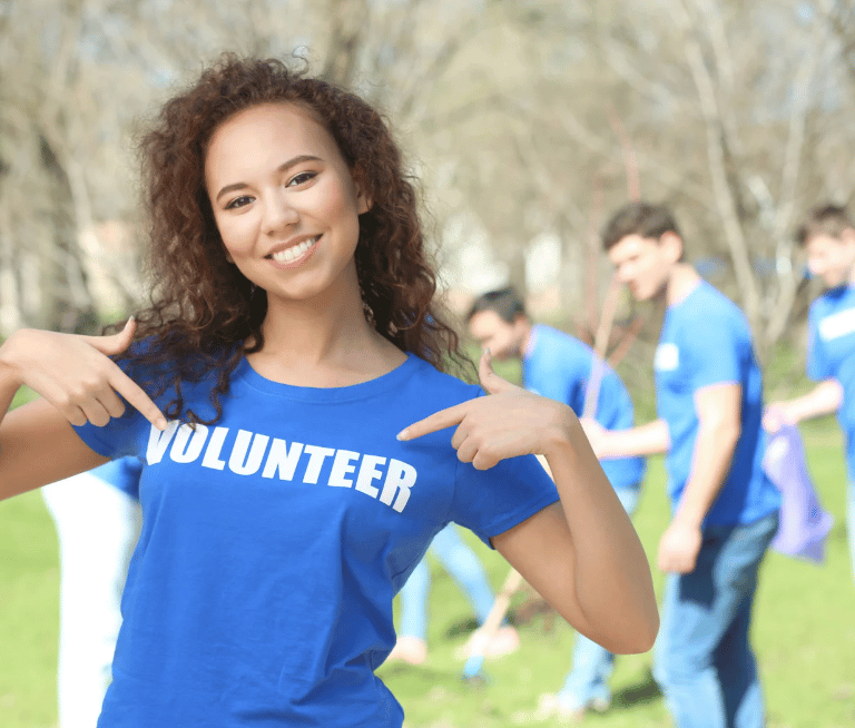 a woman in a blue shirt is pointing at her shirt that states she is a volunteer