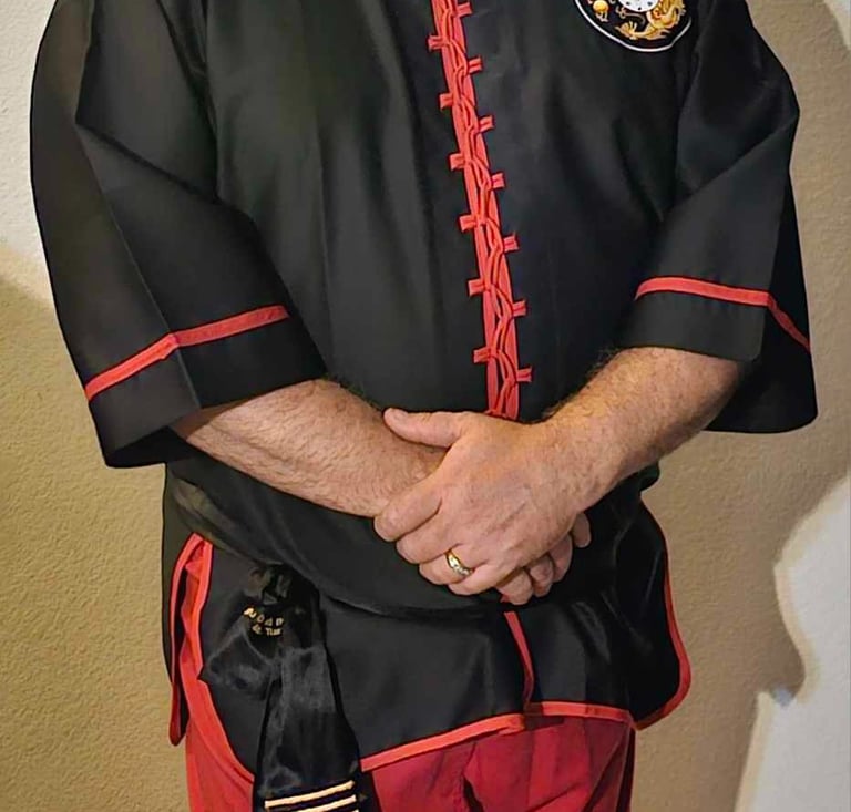 A bearded man wearing a black martial arts uniform with red trim and a gold dragon patch.