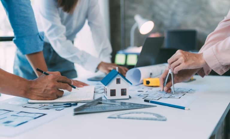 Architects working on blue prints and a house model for home design planning.