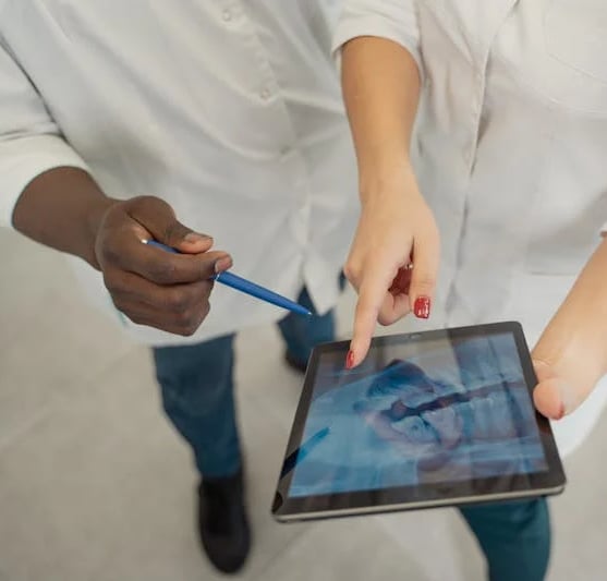 un médico con un bolígrafo y una Tablet enseñando una radiografía dental a otro odontólogo