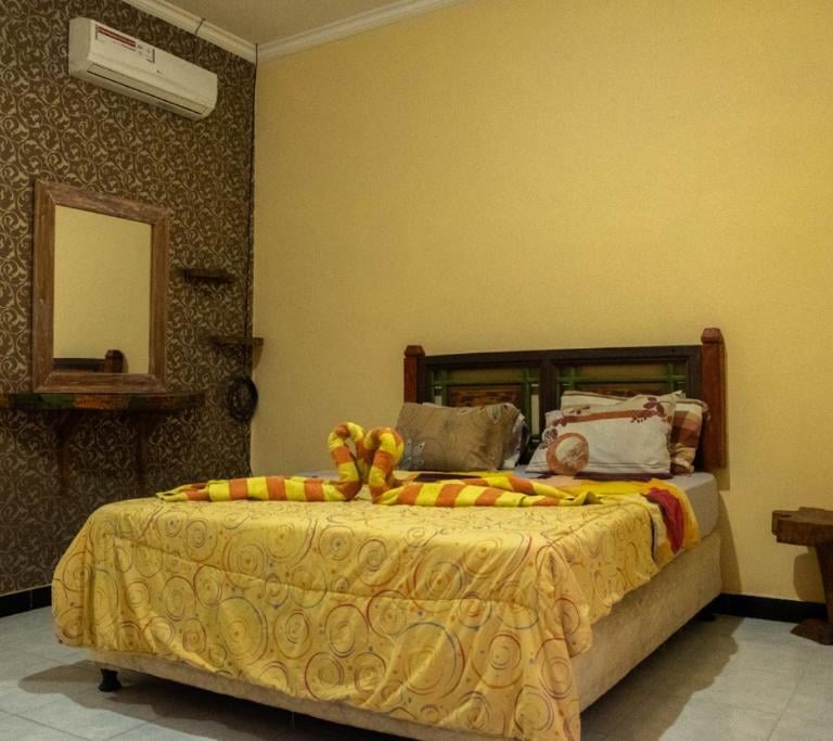 кровать с желтым постельным бельем и зеркалом наша комната в отеле Sunrise Lodge and Lovina Bali