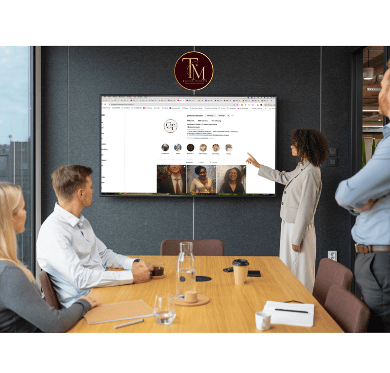 a group of people sitting around a table with a man pointing at a screen