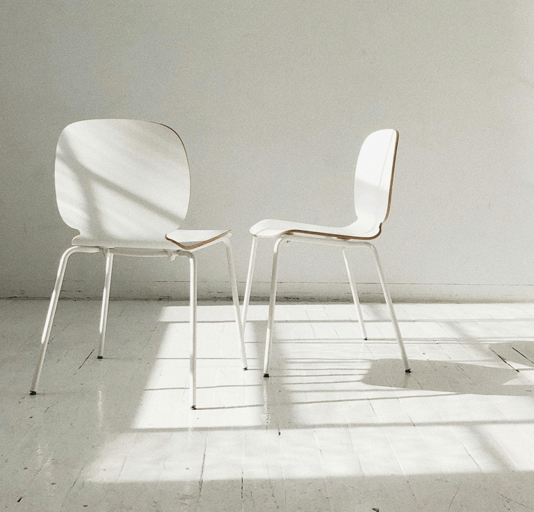 Twee witte stoelen schuin tegenover elkaar met een open ruimte ertussen, symbool voor oudercontact 