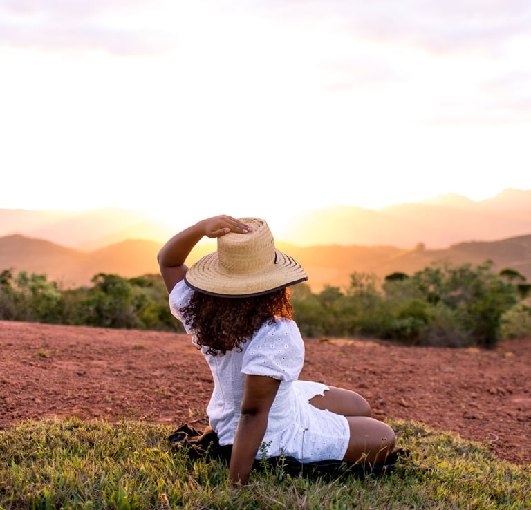 a woman in a white shirt and hat sitting on a hill