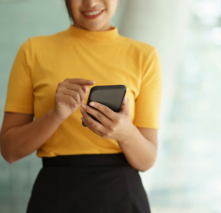 Woman in a gold top and dark brown skirt scrolling on a smart phone