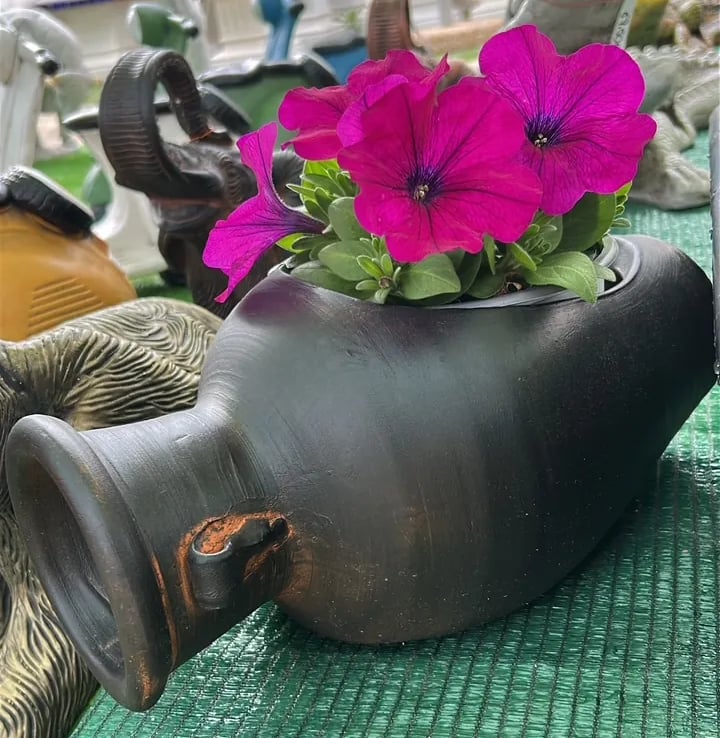 Vibrant magenta petunias blooming inside a rustic black ceramic vase at an outdoor pottery market.