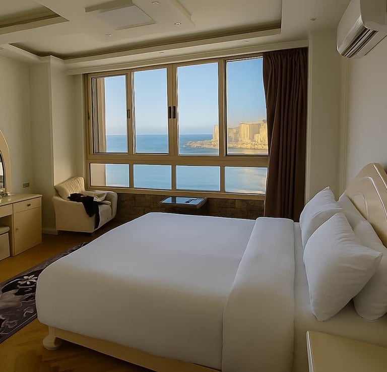 Luxury hotel bedroom with a large window overlooking the Mediterranean sea and coastal cliffs.