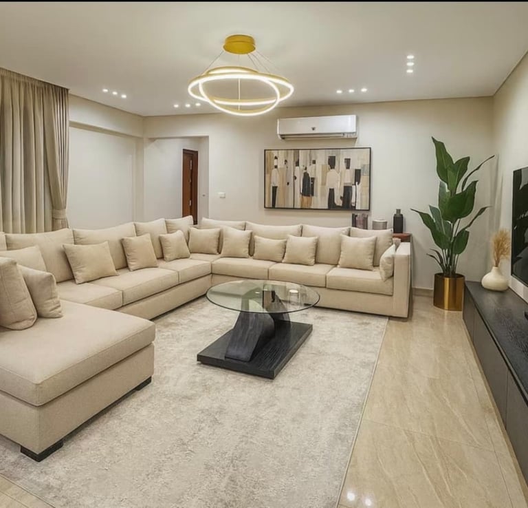 Modern living room featuring a large beige sectional sofa, glass coffee table, and flat-screen TV.