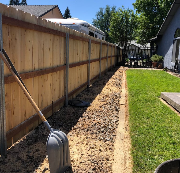 a grassy lawn with cleared area and shovel propped up against fence