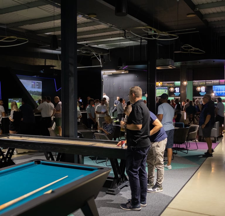 A busy event at 1IRON indoor golf simulator venue with people playing pool, shuffleboard and golf