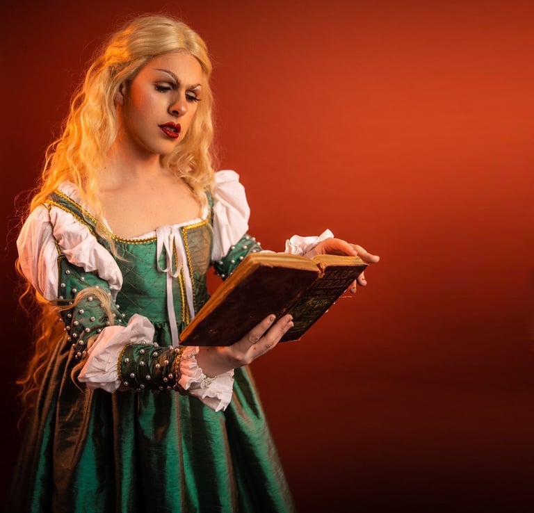 A blonde drag princess in a green and white dress reading a book. Photo credit: Owen Leavey