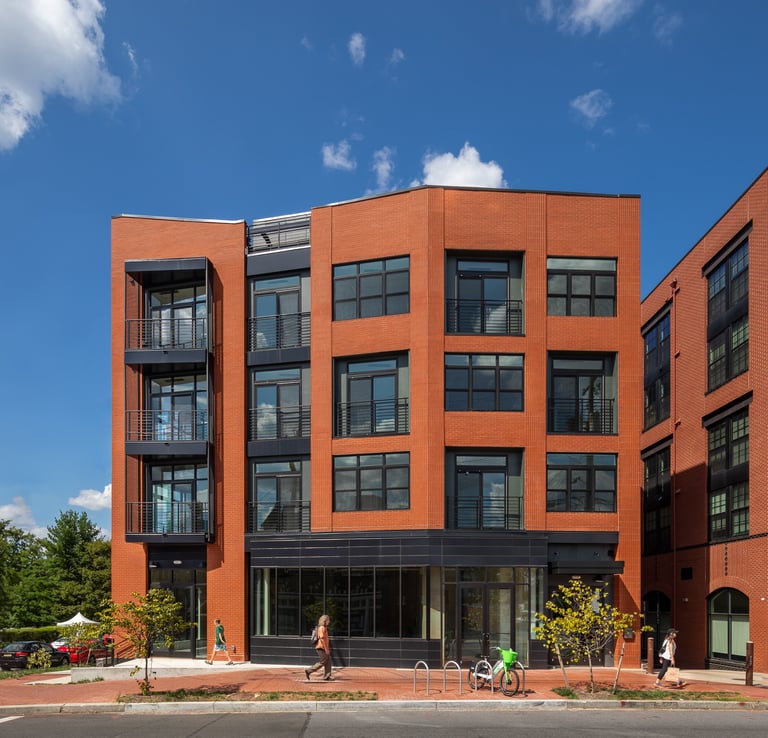 Modern red brick apartment building with black window frames and private balconies under a blue sky.