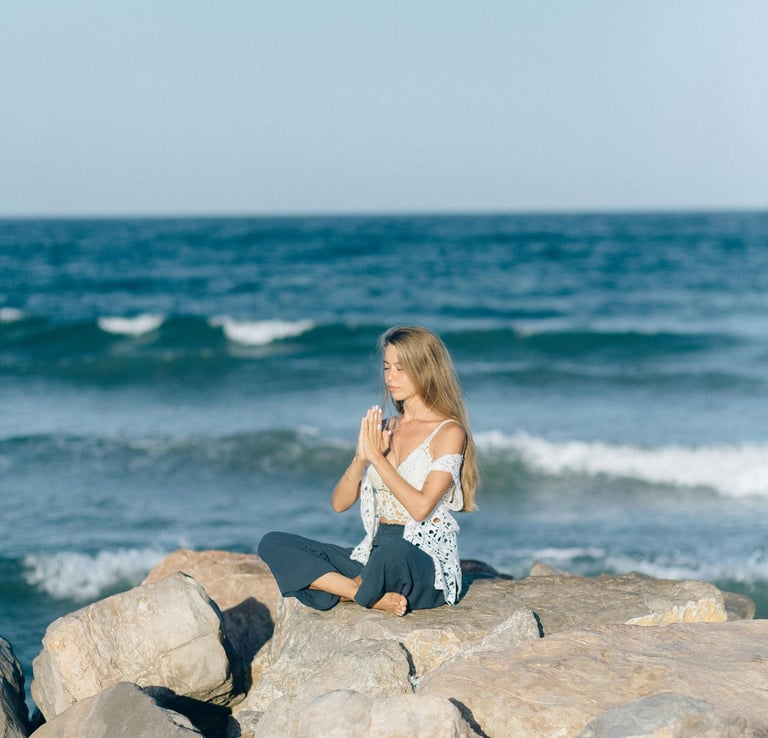 Person meditating on a rock by the ocean, representing emotional regulation and mindfulness Individu