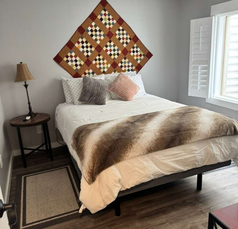 Cozy modern bedroom with a handmade quilt wall hanging and a faux fur throw on the bed.