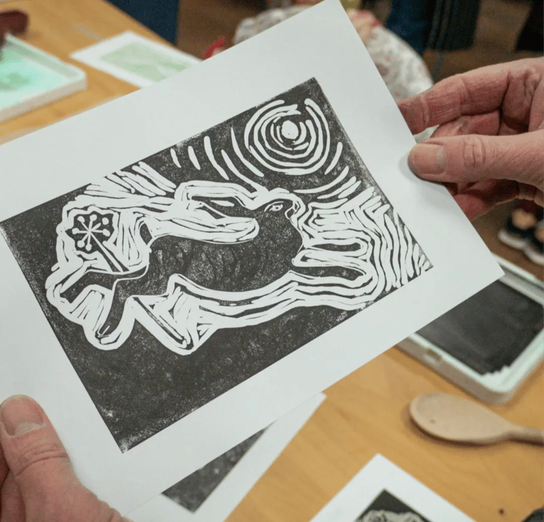 Person holding a linocut print of a hare with art workshop in background