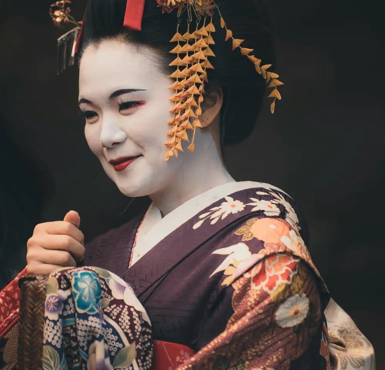 portrait of a smiling geisha or maiko (apprentice) wearing a dark purple kimono with a colorful patt