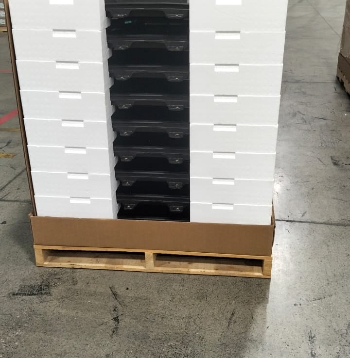 A stack of black glass panels securely packaged with white foam inserts on a wooden pallet.