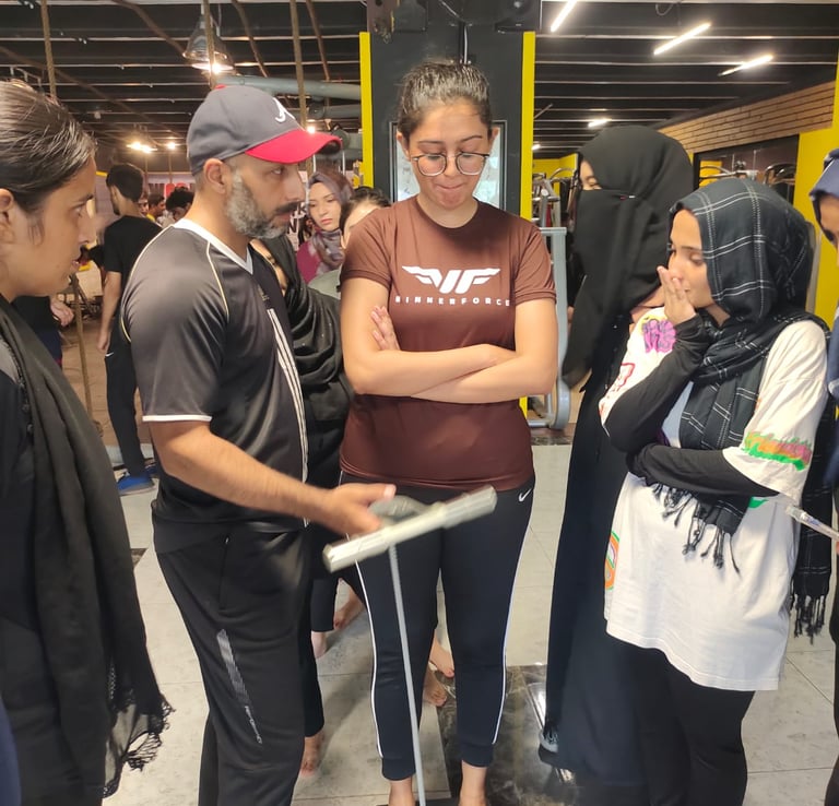 A gym trainer assists a young woman checking her on a BIA scale during a fitness assessment.