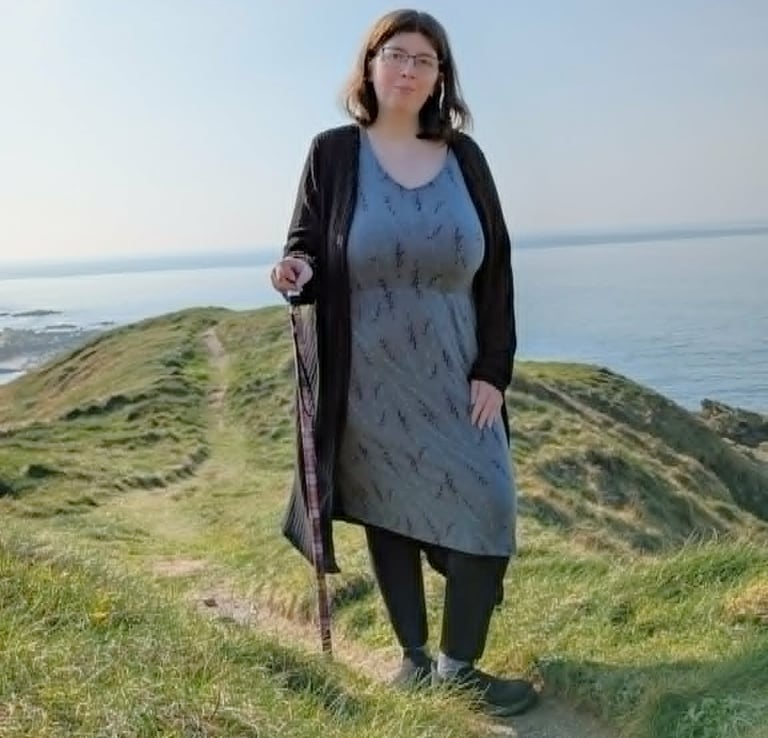 Bex standing on a coastal path with a walking stick.