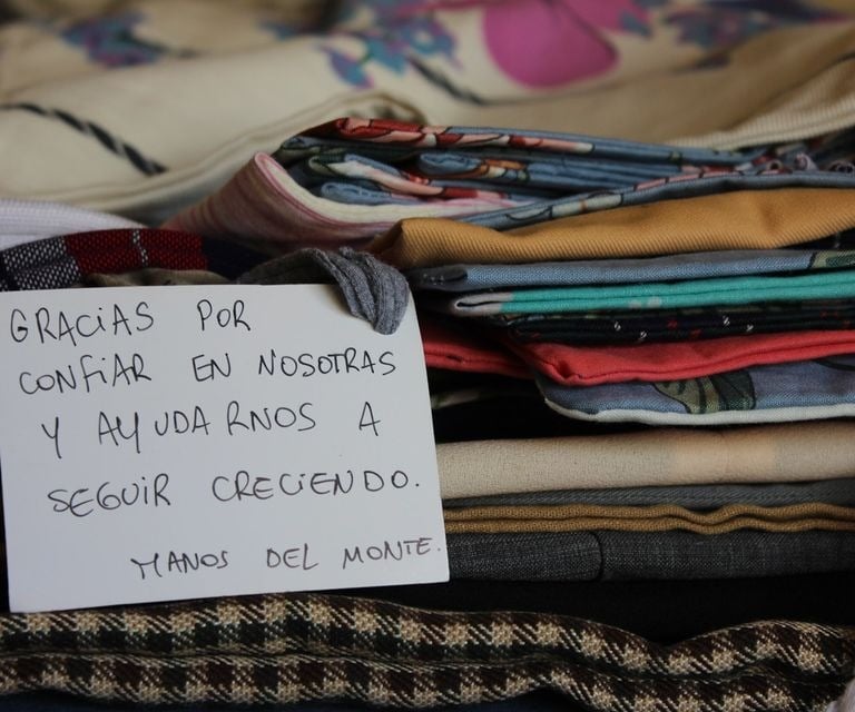 Handwritten thank you note on a stack of folded handmade textile clothing and patterned fabrics.