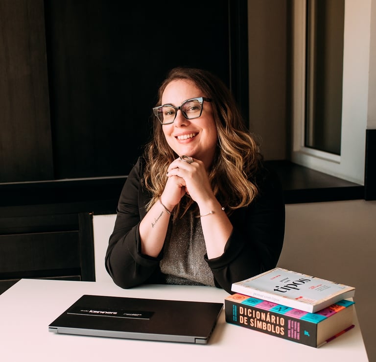 Foto da Ro Lammers sorrindo em sua mesa de trabalho, com notebook e livros.