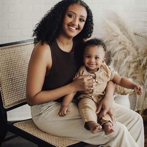 Black mother sitting with her baby on her lap, both smiling with tenderness, love, gentle grace.