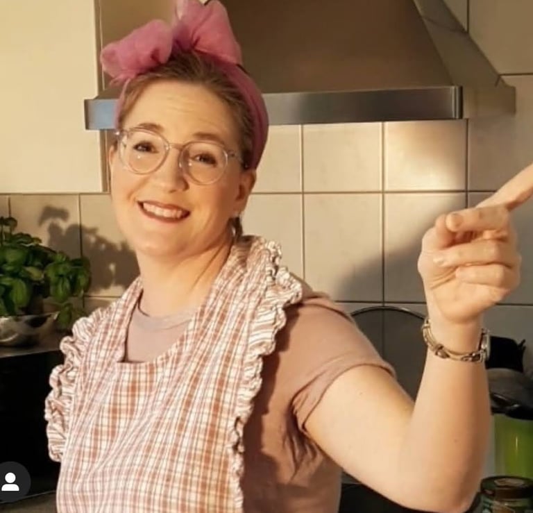 Sängerin Betti Konfetti mit pinker Haarschleife und Küchenschür2020 zu Hause während der Coronazeit.