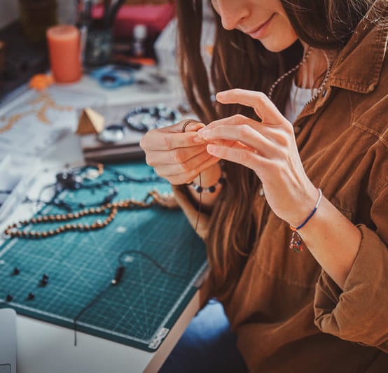 Artesano joyero elaborando un collar hecho a mano con cuentas en una mesa de trabajo.
